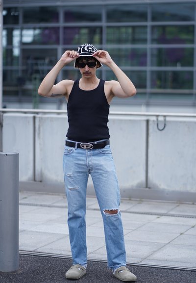 Top sin mangas negro acanalado, jeans desgastados de color azul claro, mocasines grises, gorro de punto negro con blanco, y gafas de sol negras.