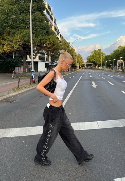 Pantalones anchos negros con bordado floral a lo largo del costado, combinados con un top corto blanco. La modelo lleva gafas y lleva un bolso negro.