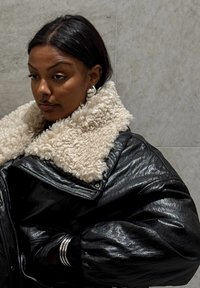 Sort læderjakke med en tekstureret cremefarvet imiteret shearling-krave. Har overdimensionerede ærmer og sølvfarvede accenter.