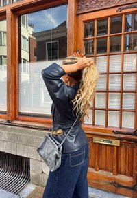 Sort læderjakke med en indsnævret talje og stort guldbeslag. Mørke denim jeans med afslappet pasform. Grå læder crossbody taske.