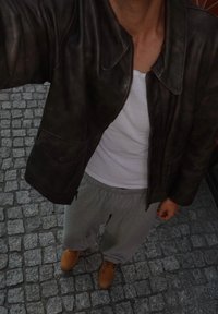 Brun lærjakke, hvit tanktopp, grå joggebukser og beige støvler. Steinen på bakken er teksturert og ujevn.