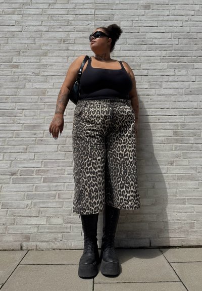 Top sin mangas negro, pantalones de pierna ancha con estampado de leopardo en beige y marrón, y botas negras de plataforma con cordones. Incluye gafas de sol y bolso de hombro.