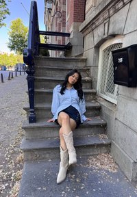 Una camicia oversize a righe blu e bianche abbinata a una minigonna di jeans scuri. L'outfit presenta stivali western chiari con motivi in rilievo.