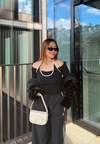 Sort off-the-shoulder top med hvide detaljer, sort pelsjakke, sorte track pants med hvide striber og en cremefarvet håndtaske. Solbrillerne fuldender looket.