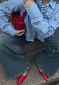 Chemise bleu clair avec accents en nœud, associée à un jean en denim évasé. Accessoirisée avec un mini sac à main rouge et des talons aiguilles rouges brillants.