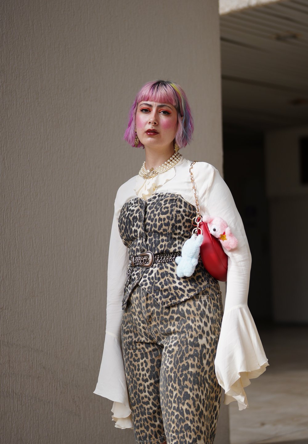 Leopardprint jumpsuit med tætsiddende overdel, hvid skjorte med klokkeærmer og kæde-bælte. Accessories inkluderer en rød taske med plyscharms.