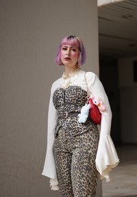 Leopardprint jumpsuit med tætsiddende overdel, hvid skjorte med klokkeærmer og kæde-bælte. Accessories inkluderer en rød taske med plyscharms.