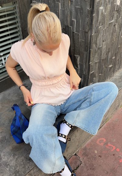 Top de color rosa claro y textura con cintura fruncida, combinado con jeans de pierna ancha de color azul claro. Bolso azul con estampado y sandalias gruesas con tachuelas.
