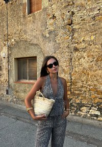 Halter top s leopardím vzorom a zladenými nohavicami v šedých tónov, doplnené tkanou béžovou kabelkou. Opozorujúca štruktúrovaná kamenná stena v pozadí.