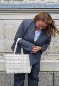 Tote torba od bijelog tkanja s dvostrukim ručkama, napravljena od glatkog materijala. Ima pravokutni oblik i rešetkast uzorak na površini.