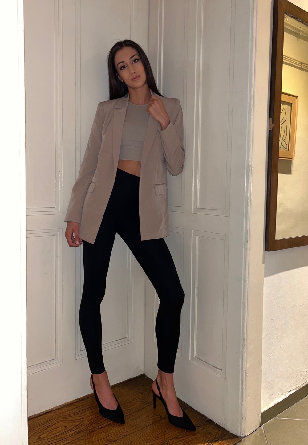 Bež blazer, črne elastične legice in črni stiletto peti. Blazer ima dve sprednji žeper, nosi se preko sive kratke majice.