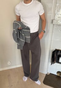 Suéter gris a rayas sostenido sobre una camiseta blanca, combinado con pantalones de chándal sueltos de color gris oscuro. Texturas notables y ajuste casual.