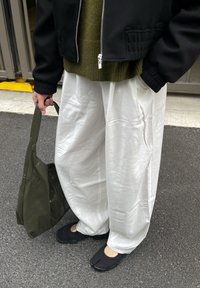 Vita vida byxor, olivgrön stickad tröja, svart bomberjacka, svarta slip-on skor och en mörkgrön väska. Släta texturer och avslappnad passform.