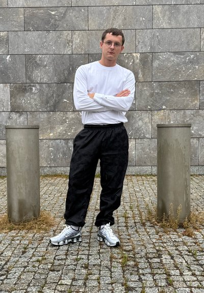 Pantalones joggers negros y texturizados con cintura elástica, combinados con una camiseta ajustada de manga larga blanca y zapatos deportivos plateados. Fondo de piedra gris.