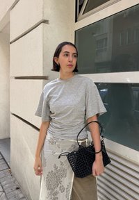 Camiseta gris de manga corta con un corte relajado, combinada con una falda envolvente de color claro con estampado y un bolso de mano de paja negra.