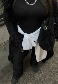 Sort bodystocking under en hvid bundet skjorte, med en lang sort pelsjakke, sorte bukser og chunky sorte sko. Sølv kædehalskæde og taske.