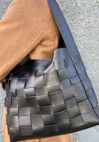 Schwarze gewebte Lederhandtasche mit strukturiertem Design, ausgestattet mit einem breiten Tragegurt und einer strukturierten Oberfläche. Zeigt ein kunstvolles Webmuster.