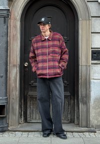 Veste en mélange de laine rayée rose et violette avec une fermeture éclair à l'avant et des poches latérales, associée à un jean ample gris foncé et des chaussures noires.