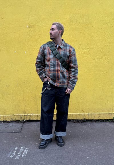 Chaqueta de cuadros en tonos gris, naranja y negro; vaqueros negros holgados con puños doblados; bolso bandolera verde; zapatos negros con detalles plateados.