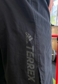 Črne atletske kratke hlače iz lahkega blaga, z logotipom Adidas in v embosiranem sivi napisu "TERREX" ob strani.