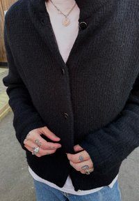 Svart strikket cardigan med en teksturert finish, med V-hals design, store svarte knapper og lange ermer. Hvit t-skjorte under.