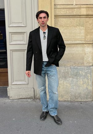 Blazer negro de doble botonadura, camiseta blanca, jeans claritos desgastados y zapatos de cuero negros. Accesorios: gafas de sol, collar con colgante.