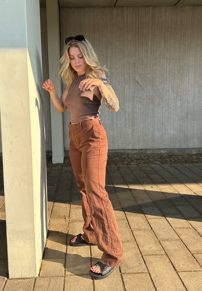 Top marrón sin mangas con un bolsillo, combinado con pantalones marrones de pierna ancha de cintura alta y sandalias negras. Texturas suaves, ajuste casual.