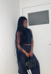 Schwarzes gestricktes Cropped-Top mit Reißverschluss, kombiniert mit hoch taillierten schwarzen Hosen. Kleine schwarze Handtasche mit goldenen Hardware-Akzenten.