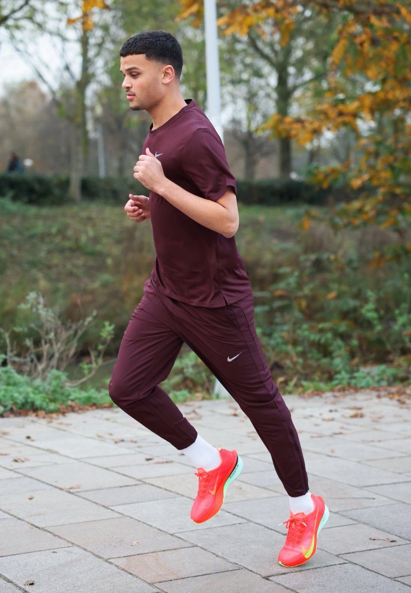 Ensemble sportif comprenant un t-shirt à manches courtes bordeaux et un pantalon de jogging assorti, accompagné de chaussures de course orange vif et de chaussettes blanches.
