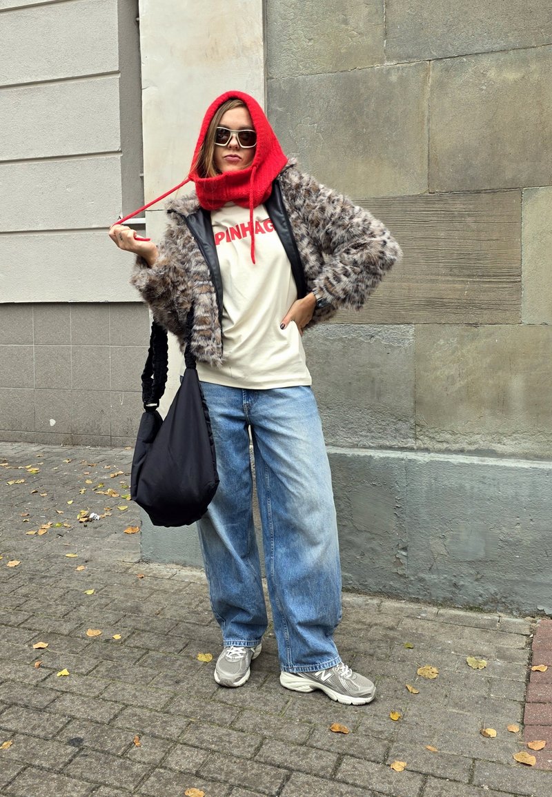 Faux fur jacket with a black leather front, red hooded scarf, beige t-shirt featuring red text, loose blue jeans, and grey sneakers. Black bag.