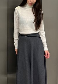 Maglione a maniche lunghe di color crema chiaro abbinato a una gonna a trapezio grigia scura con una leggera trama e una cintura nera.