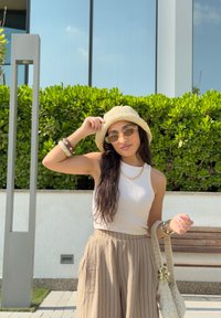 Világos bézs színű crop top és csíkos, magas derekú barna nadrág. Kiegészítők: fonott bézs kalap és napszemüveg. Texturált kézitáska.