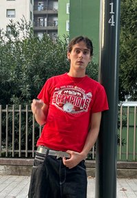 Piros póló "Ohio State Buckeyes" és "Bajnokok" felirattal, fekete farmernadrággal párosítva. Ezüst öv csillag alakú csattal, egy póznának dőlve.