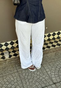 Pantaloni bianchi in lino, morbidi e largi, con una texture stropicciata abbinati a sandali bianchi. Lo sfondo presenta piastrelle a diamante nere e crema.