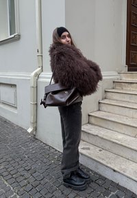 Manteau en fausse fourrure marron duveteux, jean denim foncé, chaussures compensées noires, et sac à main en cuir marron avec rabat et détail en métal.
