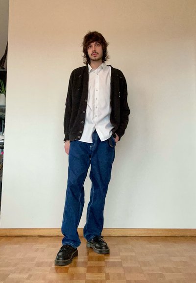 Cárdigan negro sobre una camisa blanca de botones, combinado con jeans holgados azules y zapatos de plataforma negros. Textura suave, corte suelto, estilo casual.