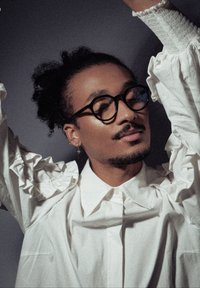 Λευκό πουκάμισο με ρυτιδωτά μανίκια, καλοσχηματισμένο γιακά και κουμπιά μπροστά. Το μοντέλο φοράει στρογγυλά γυαλιά και σκουλαρίκι, υφασμένο με μαλακό υλικό.