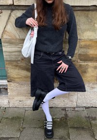 Suéter preto tricotado, calções de ganga pretos largos, meias brancas, sapatos de plataforma pretos com tiras studded e uma bolsa branca com um pendente.