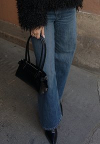 Borsa nera con effetto coccodrillo e superficie testurizzata, manici doppi; abbinata a jeans blu a gamba larga e tacchi neri appuntiti.