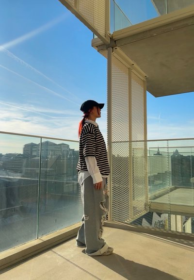 Camisa de rayas blanca y negra oversized sobre una camiseta de manga larga blanca, combinada con pantalones de chándal grises desgastados y zapatillas blancas. Gorra negra.