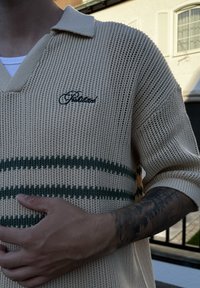 Beidzot adīts polo džemperis ar V veida kaklu, ar zaļām horizontālām svītrām un izbrokētu "Palace" logo uz krūtīm. Audums ir vaļēja adījuma.
