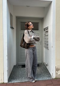 Szary, oversize sweter z kołnierzykiem, w połączeniu z luźnymi szarymi spodniami. Brązowa torba na ramię i minimalistyczne czarne okulary, na tle jasnej ściany.