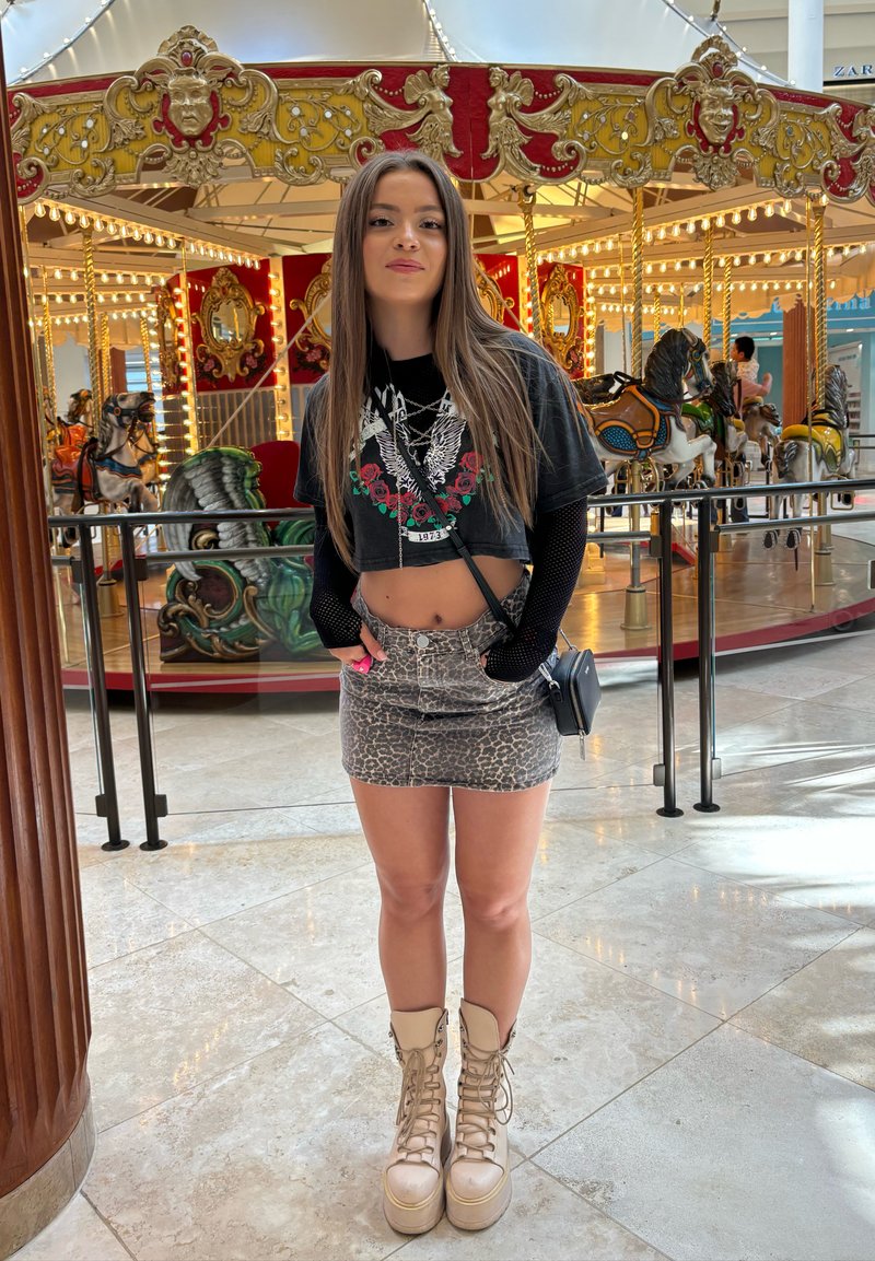 Svart kortermet t-skjorte med grafisk design og blomsterdetaljer, leopardmønstret miniskjørt, beige platå snørebott, og liten svart crossover-veske.