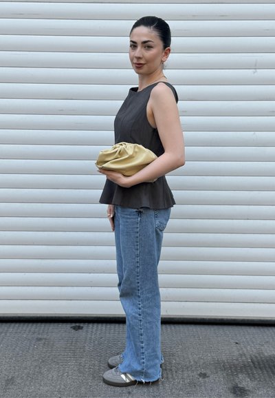 Top gris sin mangas con diseño de peplum, jeans azul de talle alto y clutch dorado claro. Zapatillas con acentos en gris y blanco.