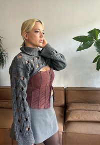 Maglione grigio a maglia con dettagli a intaglio, top corsetto bordeaux e gonna grigia. Texture liscia e a coste; outfit casual, a strati.