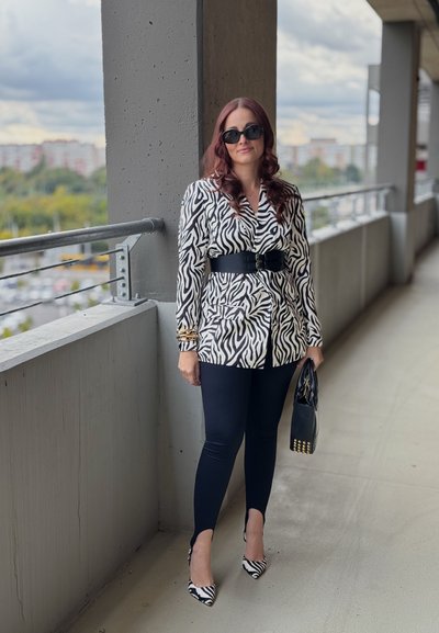 Blazer de estampado de cebra en blanco y negro con cintura ajustada, combinado con leggings negros y tacones de estampado de cebra. Los accesorios incluyen un bolso negro.