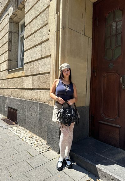 Bolso negro con cadenas, falda mini gris, medias blancas con estampado y top de tirantes azul marino. Persona con gorra clara y accesorios plateados.
