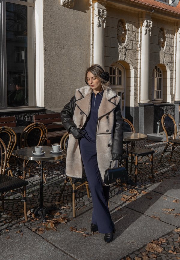 Dvojradový kabát z ovčej vlny v béžovej a čiernej farbe s veľkými klopami, skombinovaný s námorníckym overalom a čiernymi rukavicami. Súčasťou je aj malá kabelka.