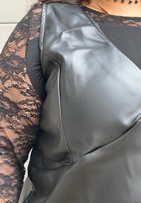 Czarna odzież z sztucznej skóry charakteryzująca się eleganckim wzornictwem, z teksturowaną bluzką z długim rękawem z koronką pod spodem. Podkreśla gładkie linie i dopasowanie.
