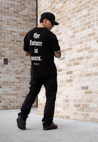 Black t-shirt featuring large white text "the future is ours. Dropsize" on the back, teamed with black cargo trousers and brown trainers.